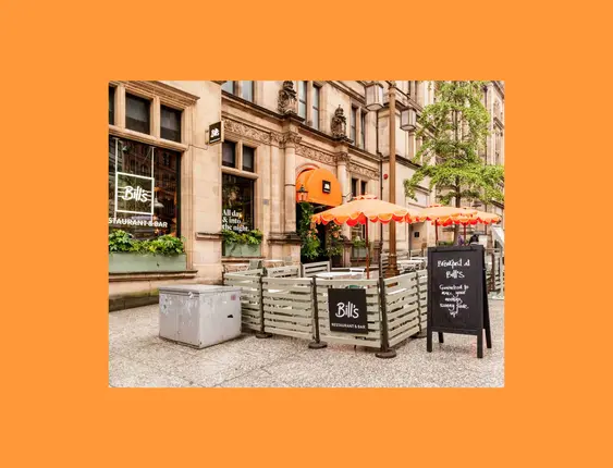 Street view of Bill's Restaurant & Bar with outdoor seating and bright orange umbrellas.