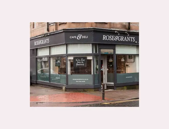 Rose &amp; Grants Cafe &amp; Deli corner facade with large windows and signage, under a cloudy sky.