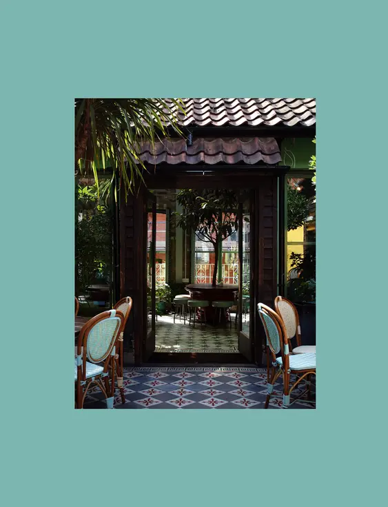 Tranquil garden café with tropical plants, patterned tiles, and inviting open doors.