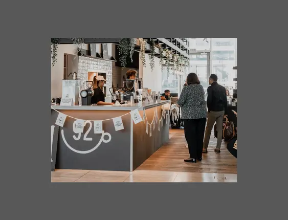 Interior of a bustling coffee shop with customers and staff, a long counter with coffee machines and decorations, and a sign promoting free coffees.
