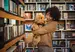 Happy woman with black hair wearing sweater with her goldendoodle therapy dog in library