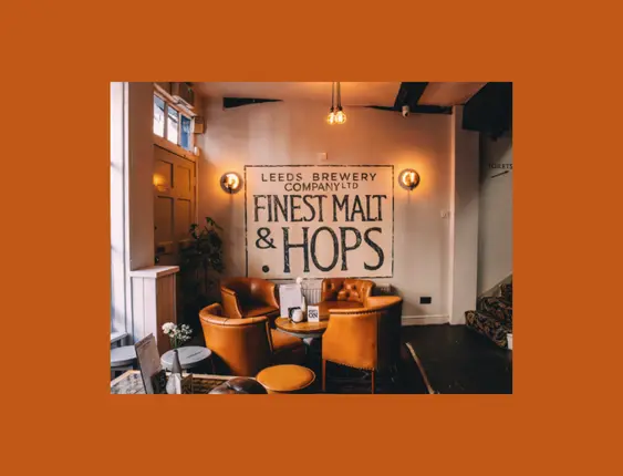Warm pub interior with leather armchairs, under a sign reading 'Leeds Brewery Company Ltd Finest Malt & Hops'.