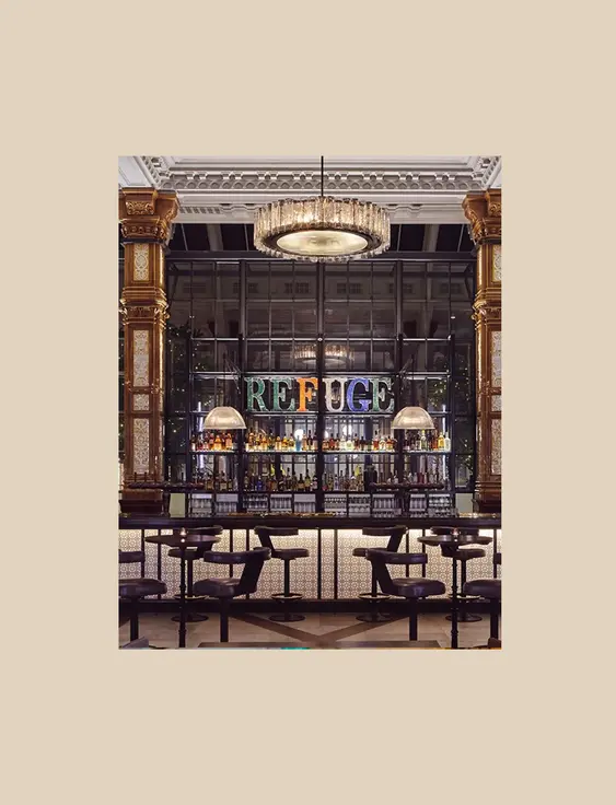 Opulent bar interior with ornate golden columns and intricate tiled pillars, featuring a well-lit bar counter, plush seating, and a 'REFUGE' neon sign in the background.