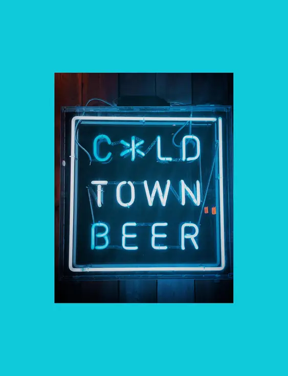 Neon sign reading "Cold Town Beer" mounted on a dark wooden wall, glowing in blue and white.