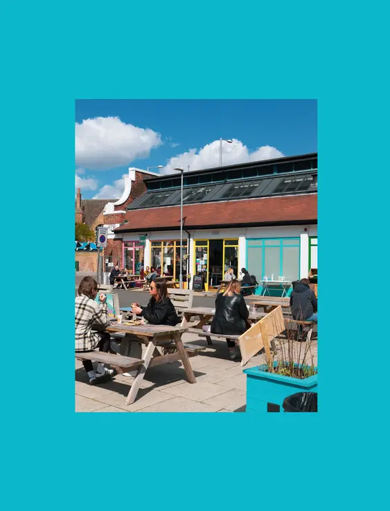 Outdoor café scene with people dining at picnic tables under a sunny sky.