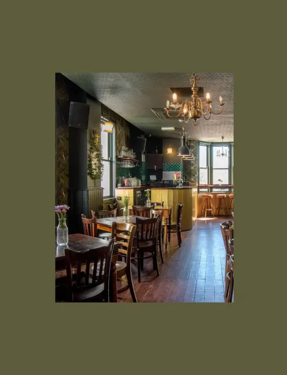 Inside of a bar with green patterned wallpaper, wooden tables and chairs.