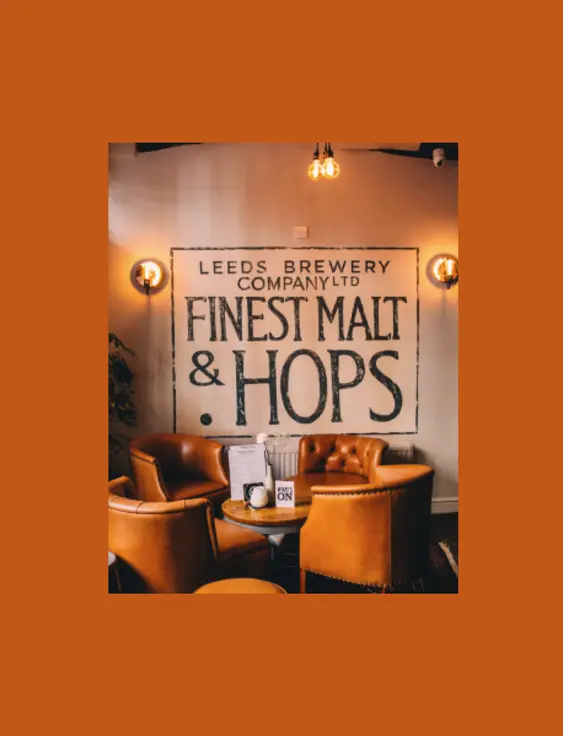 Warm pub interior with leather armchairs, under a sign reading 'Leeds Brewery Company Ltd Finest Malt & Hops'.