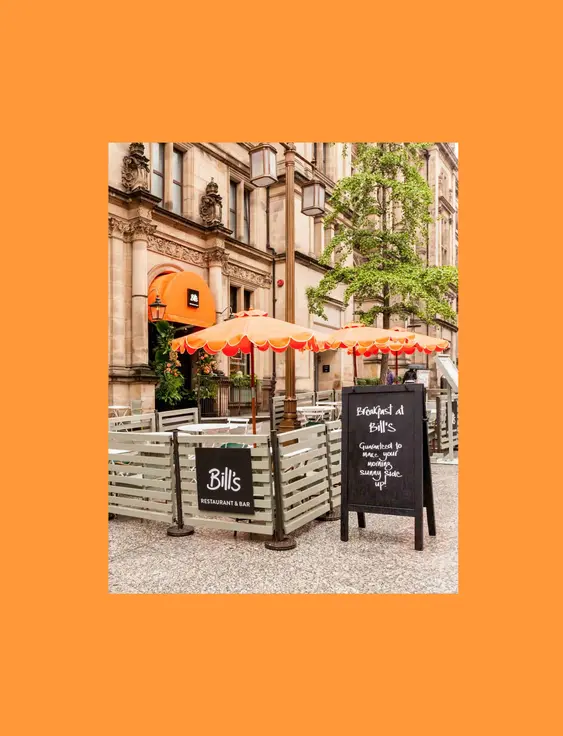 Street view of Bill's Restaurant & Bar with outdoor seating and bright orange umbrellas.