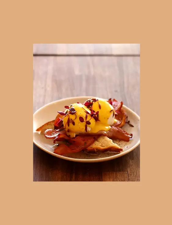 Eggs benedict on toast garnished with red leaves.