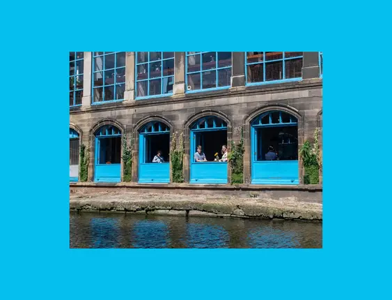 Waterfront café with vibrant blue window frames and patrons enjoying the view.