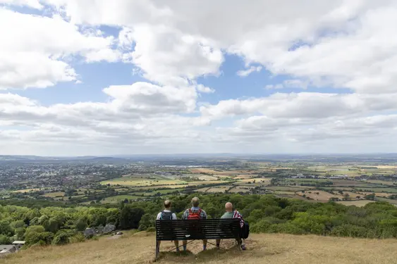 Three men look down on Cheltenham while sat on a bench on the Costswolds Way