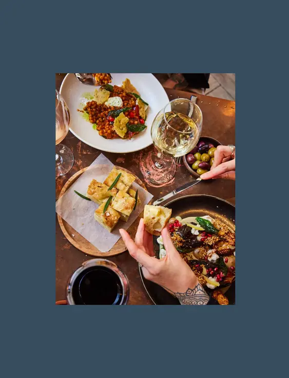 Hands reaching into table of food and wine.