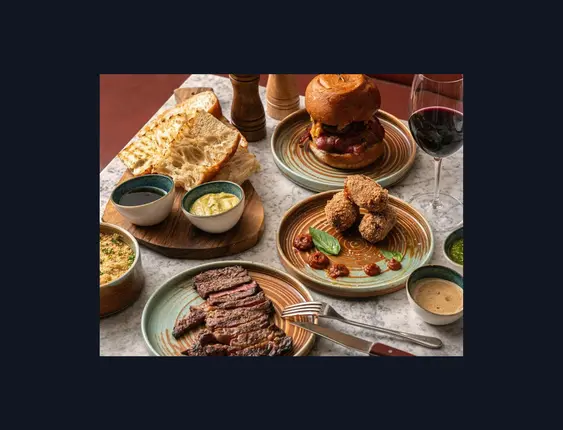 mix of food on marbled table including steak and a glass of red wine