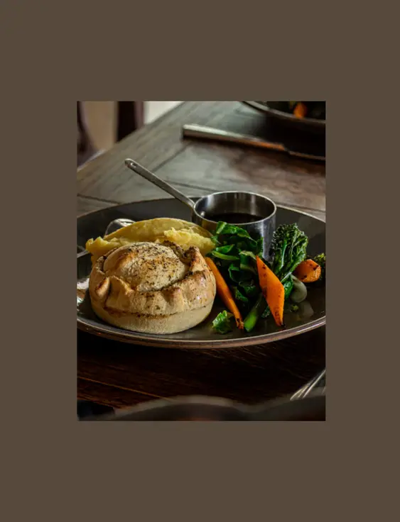 Pie, mash, vegetables and gravy on a plate, on a dark wood table.