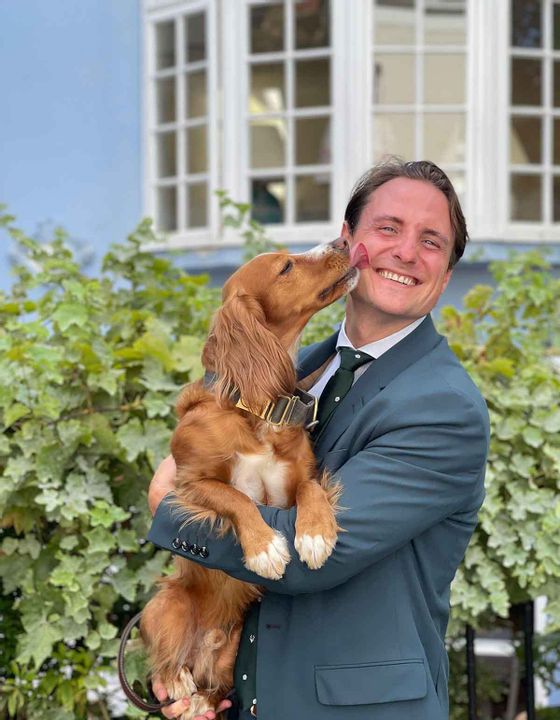 Image of Toby Brown, Director of TLC London, holding a brown dog who is licking their face