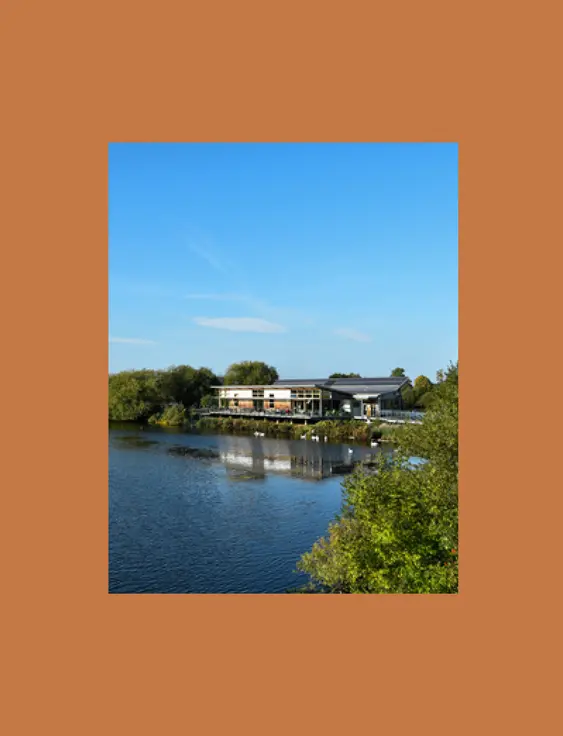 Modern visitor centre surrounded by a serene lake and lush greenery.