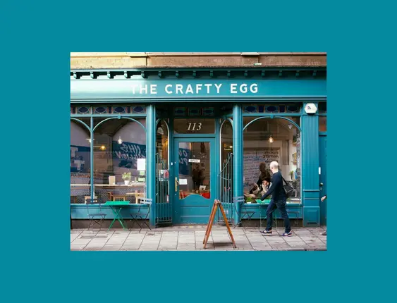 The blue front of the crafty egg cafe with a man walking across the front.