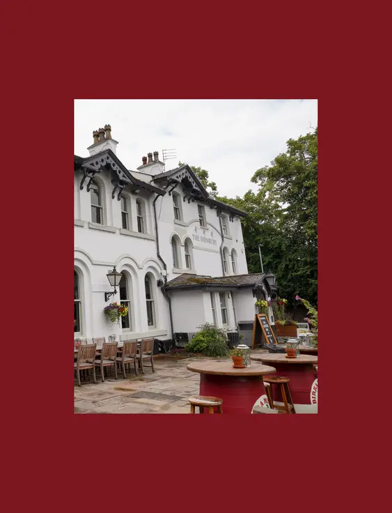 White historic pub building, "The Didsbury," with outdoor seating and arch windows under a cloudy sky.