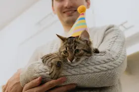Man in oatmeal sweater holding a cat in a birthday hat