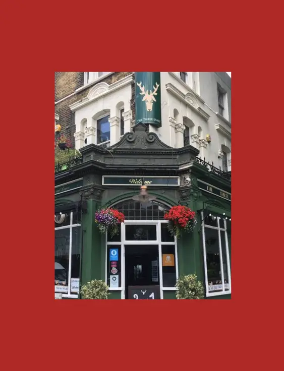 Traditional British pub on a corner, with vibrant flower baskets and '2 for 1 Cocktails' offer. The green facade stands out under a clear sky, inviting guests to its outdoor seating area.
