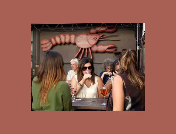 People drinking wine on a pub bench with a lobster on the wall in the background.
