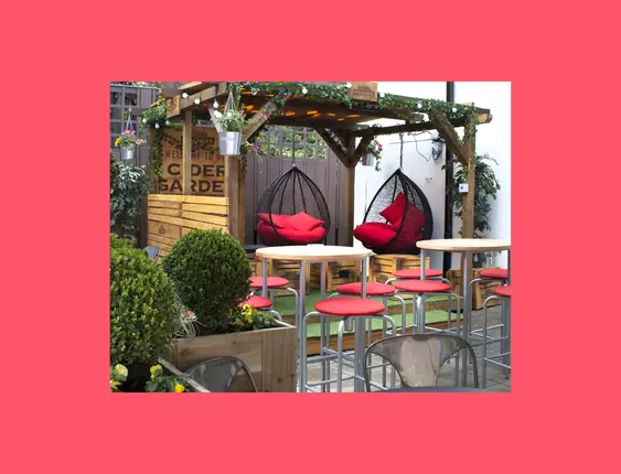 Cosy outdoor pub garden with vibrant red chairs, hanging swing seats, and lush greenery under a canopy.