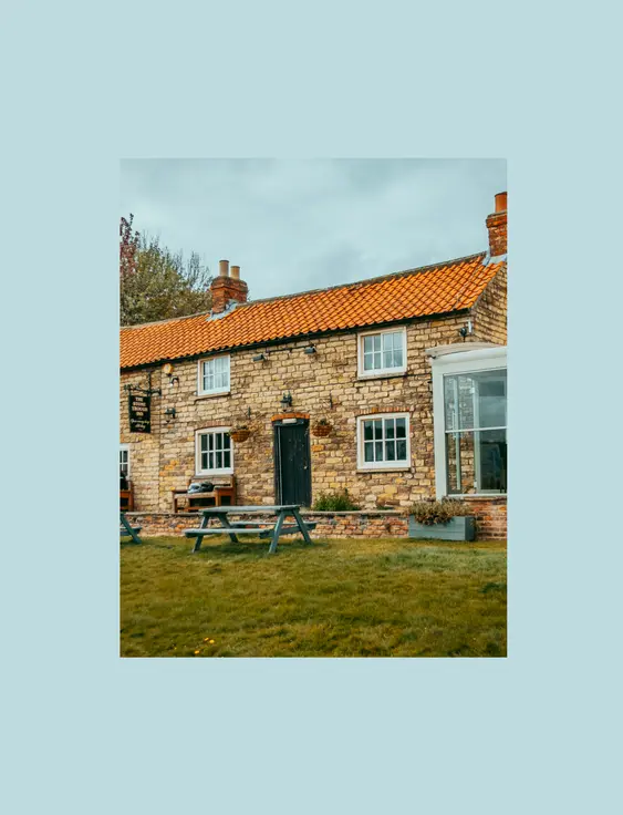 The front of the stone trough inn pub, and a green a the front with a blue bench on it.