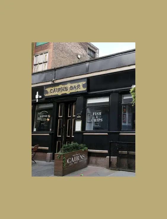 Exterior view of Cairns Bar, featuring a black facade with gold lettering and Scottish ale and fish + chip offerings.