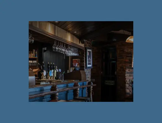 Pub interior with blue bar, hanging glasses and brick walls.