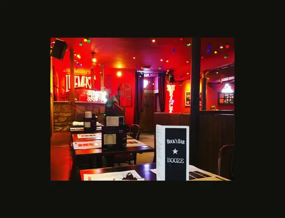 Vibrant bar interior with red lighting, neon signs, and colourful hanging bulbs over wooden tables.
