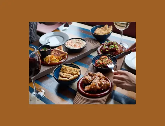 A table filled with diverse dishes and glasses of wine, shared by people dining together.