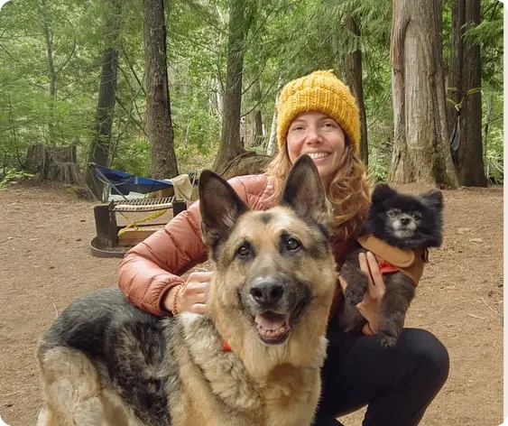 Woman kneels in woods with loyal German Shepherd and cute Pomeranian.