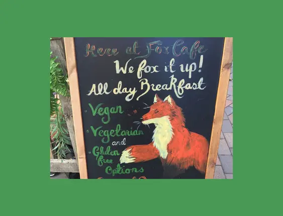 Chalkboard menu at Fox Café advertising vegan, vegetarian, and gluten-free options, decorated with a painted fox.