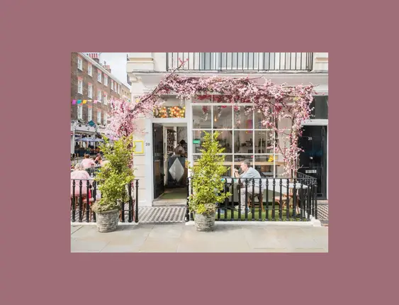 Charming corner café with outdoor seating, adorned with blooming purple wisteria, where patrons enjoy conversation on a city street.