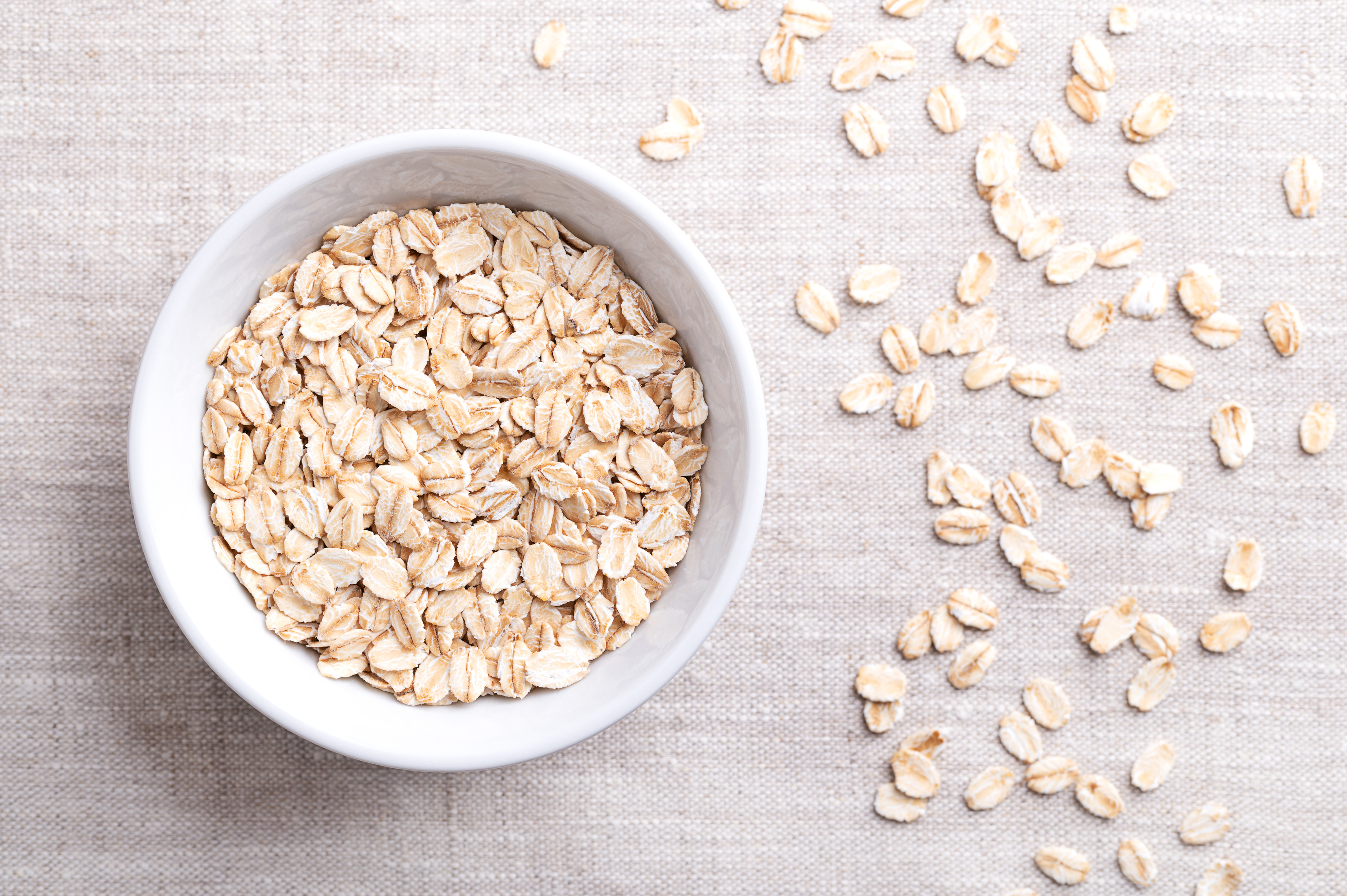 A bowl of raw oats with individual oats lined up next to it