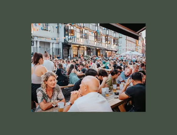 Lots of people sat drinking on pub benches in busy street