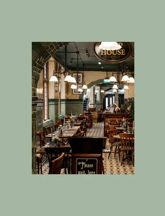 Victorian-style restaurant interior with green tiled walls and archways, featuring a long dining area with wooden tables and hanging lights.
