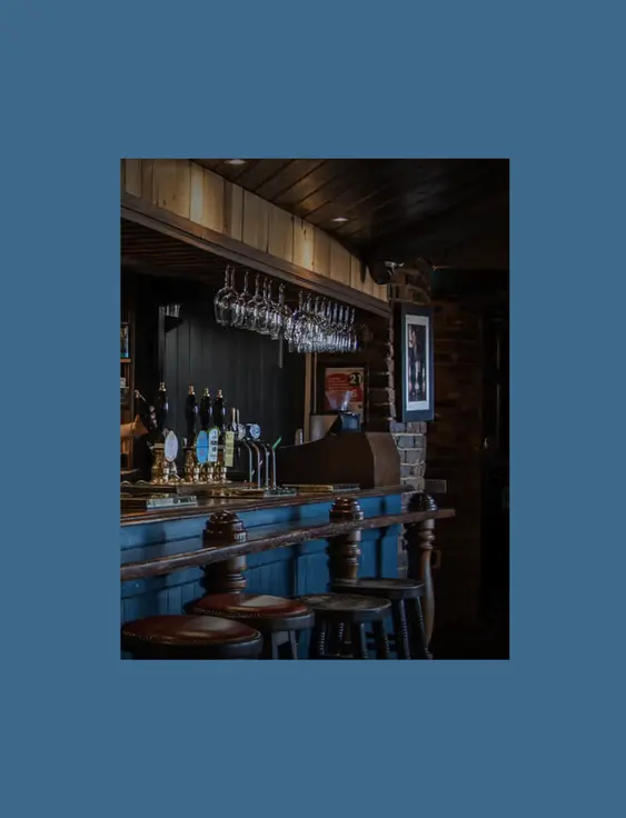 Pub interior with blue bar, hanging glasses and brick walls.