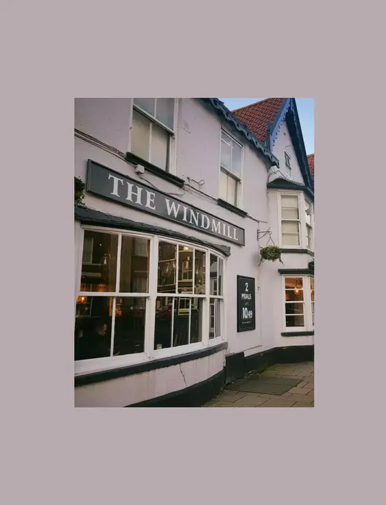 Front of a white pub with a black sign above the window that says 'the windmill'.