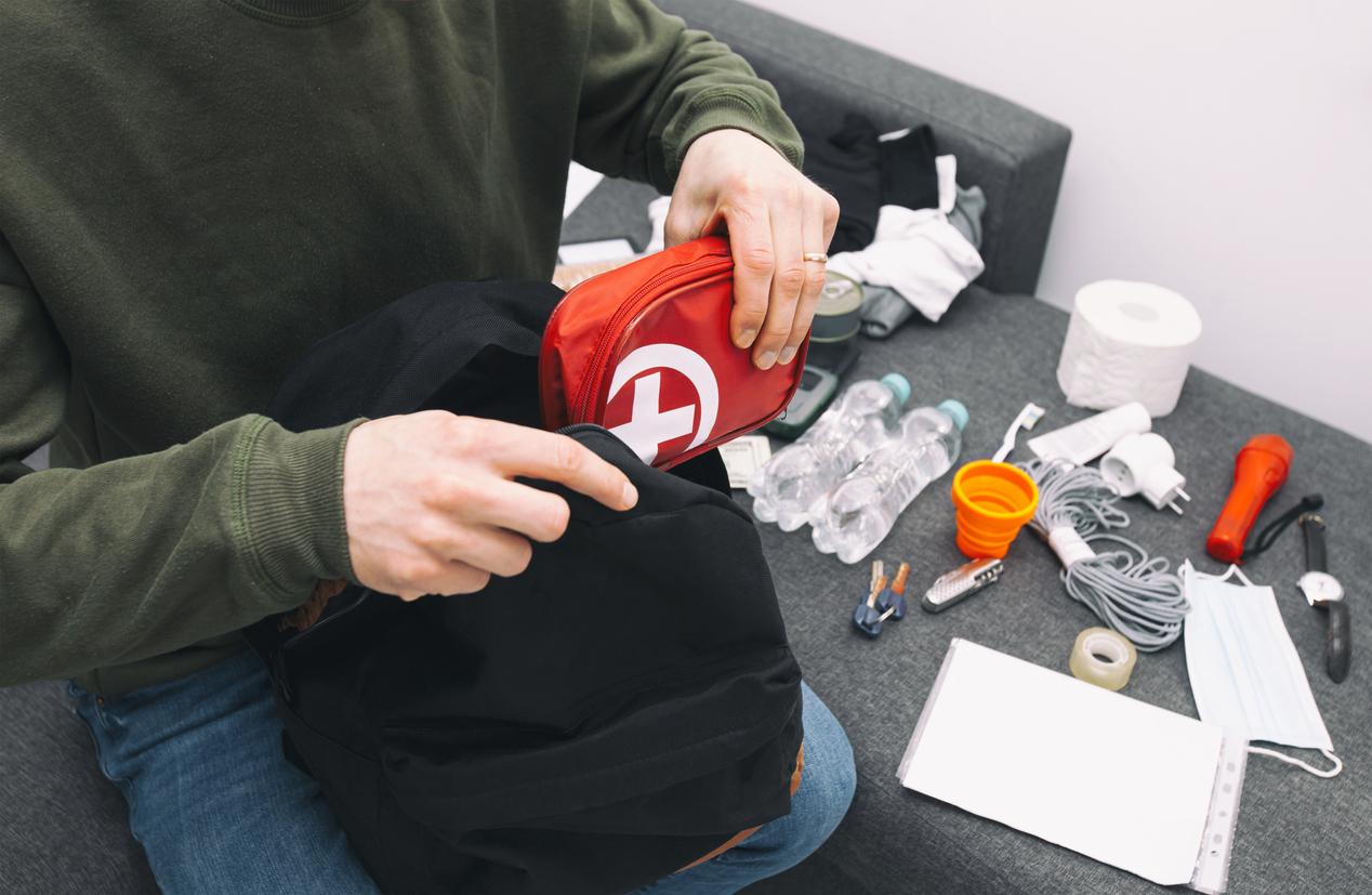 Young man packing the bag with documents, water,food, first aid kit and other items needed to survive
