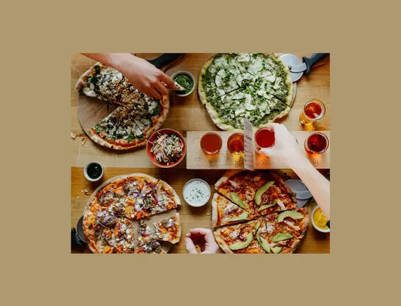 Two hands reaching in towards a table of pizza and cider.