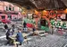 A vibrant outdoor seating area under a railway arch in Manchester, featuring graffiti walls and picnic tables. Patrons chat and dine outside the Thirsty Scholar pub, highlighted by its colorful signage.