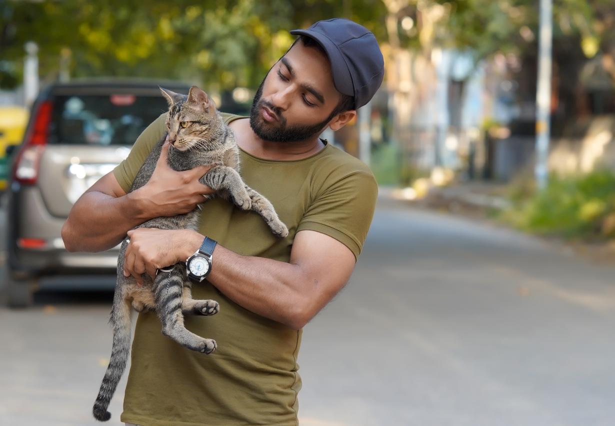 man wearing baseball cap holds cat outside