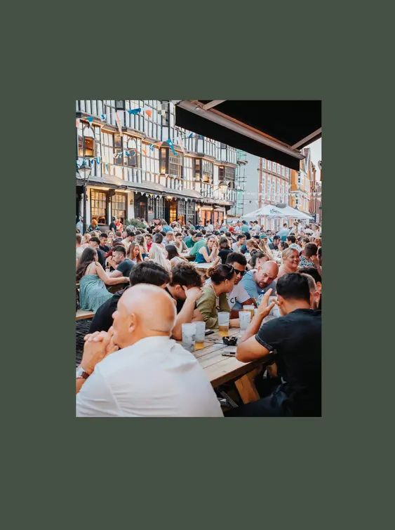 Lots of people sat drinking on pub benches in busy street