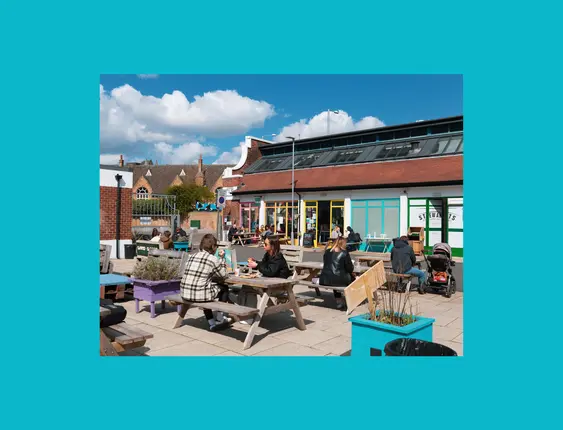 Outdoor café scene with people dining at picnic tables under a sunny sky.