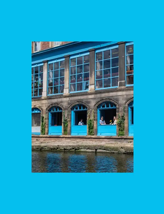 Waterfront café with vibrant blue window frames and patrons enjoying the view.