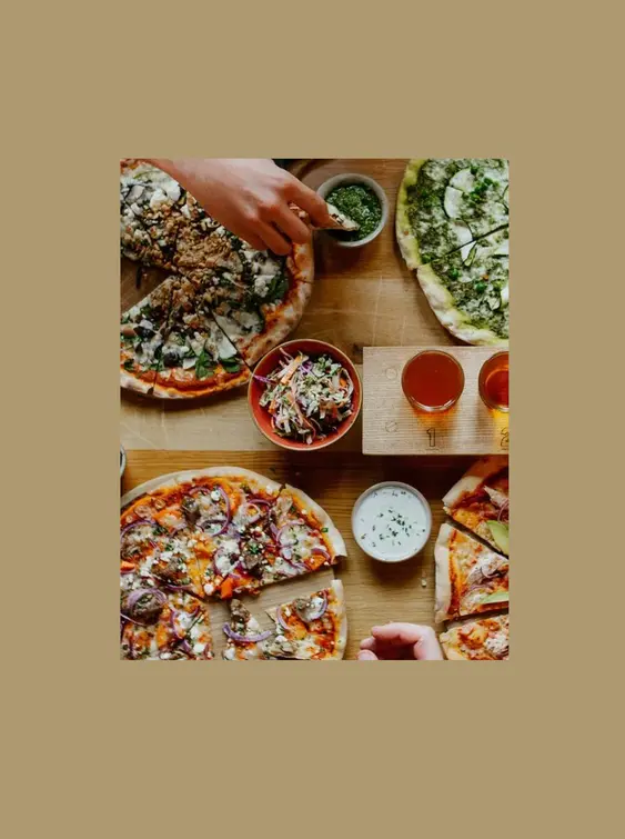 Two hands reaching in towards a table of pizza and cider.