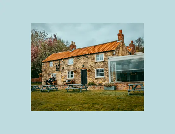 The front of the stone trough inn pub, and a green a the front with a blue bench on it.