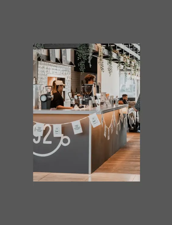 Interior of a bustling coffee shop with customers and staff, a long counter with coffee machines and decorations, and a sign promoting free coffees.