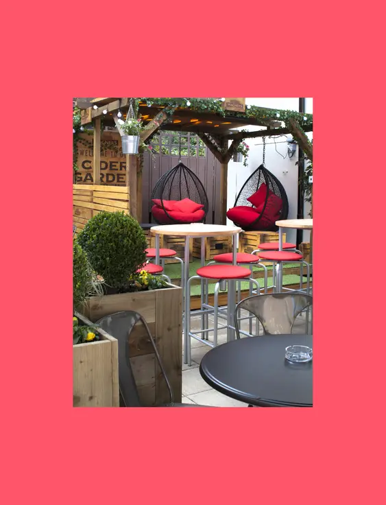 Cosy outdoor pub garden with vibrant red chairs, hanging swing seats, and lush greenery under a canopy.